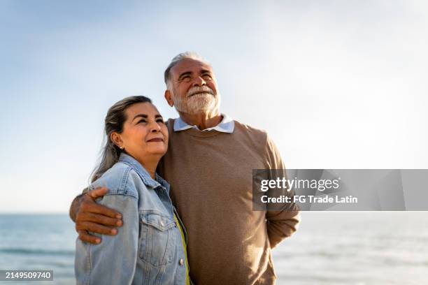 senior couple looking away admiring the view on the beach - verlangen stockfoto's en -beelden
