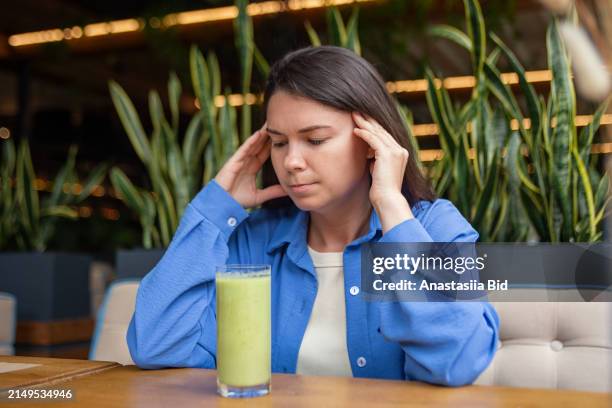 young woman with headache sitting in the restaurant.green smoothie near her at the table. - anorexia nervosa stock pictures, royalty-free photos & images