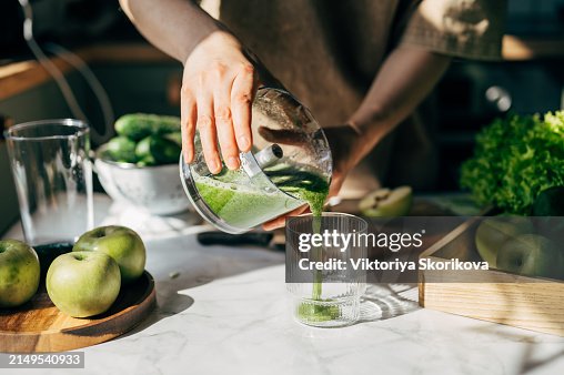 Young Woman Making Detox Smoothie At Home. Woman pouring smoothie to glass. healthy food concept Young Woman Making Detox Smoothie At Home. Woman pouring smoothie to glass. healthy food concept