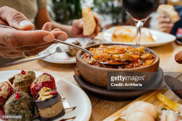 traditional georgian cuisine. man eating vegetarian chashushuli with mushrooms, with phali - snack made of nuts, various vegetables or herbs and spices and eggplant rolls,  lobio in clay pot and pickled vegetables, and a glass of red wine on background. - georgian man stock pictures, royalty-free photos & images