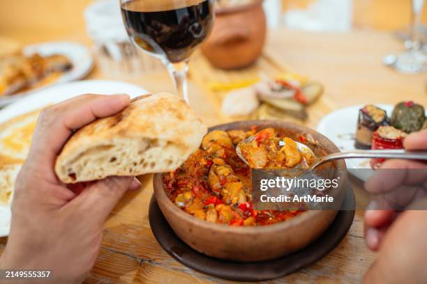 traditional georgian cuisine. man eating vegetarian chashushuli with mushrooms, with phali - snack made of nuts, various vegetables or herbs and spices and eggplant rolls, lobio in clay pot and pickled vegetables, and a glass of red wine on background. - geórgia cáucaso do sul imagens e fotografias de stock