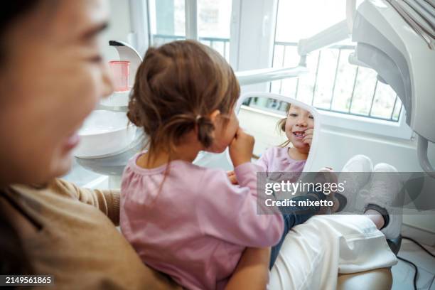 cute little girl having fun while looking at the mirror at dentist's office - kinderzahnheilkunde stock-fotos und bilder