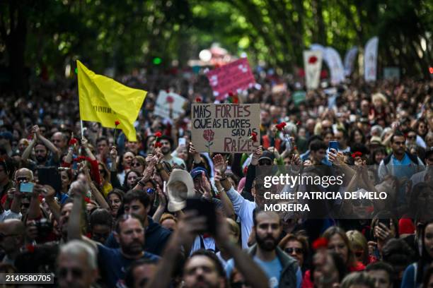 Woman holds a placard reading "Stronger than flowers are roots" as people demonstrate during the Carnation Revolution's 50th anniversary at Avenida...