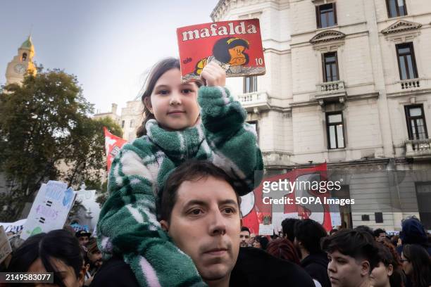 Little girl on her father's shoulders lifts the book of Mafalda, a classic Argentine cartoon during the rally. Protesters in favor of public and free...