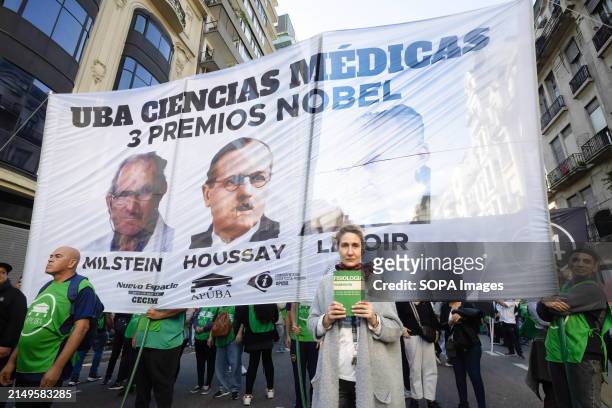 Woman holds a book in her hand, in front of a poster with the three Argentine Nobel Prize winners: Milstein, Houssay and Leloir during the rally....