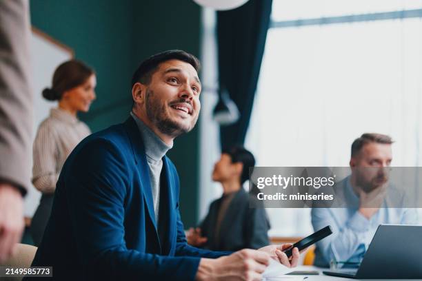 un felice e bellissimo uomo d'affari che distoglie lo sguardo mentre lavora in ufficio - colore brillante foto e immagini stock