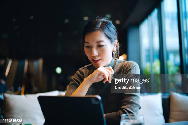 young asian businesswoman looking at her digital tablet while sitting at a desk in stylish co-working space and working. successful female entrepreneur and leadership. technology in a modern lifestyle. working remotely with flexibility - finansiell rådgivare bildbanksfoton och bilder