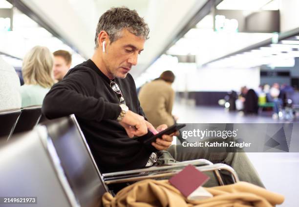 man waiting at airport departure gate, using smartphone - flughafen wien stock-fotos und bilder