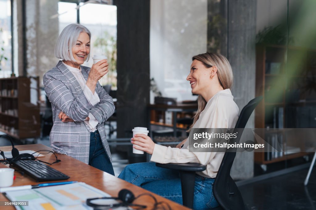 Short break during workday, coffee from younger colleague. Friendship in workplace between colleagues in various age groups in office. Age diverse team concept.