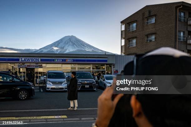 This photo taken on January 1, 2024 shows a tourist posing in front of a convenience store with Mount Fuji in the background, in the town of...