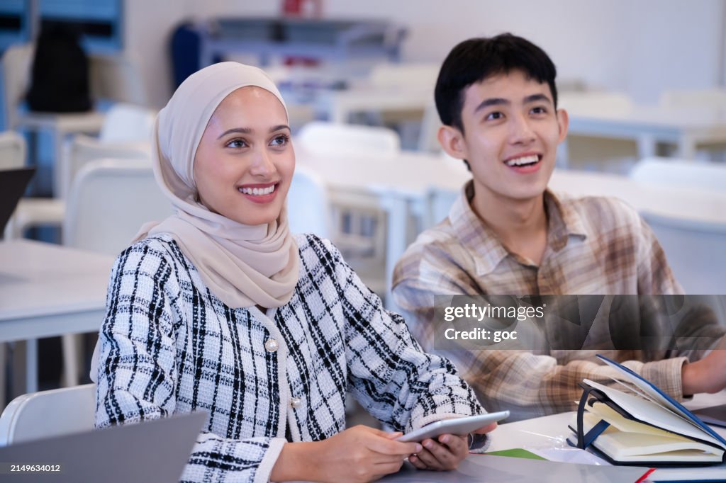 Two multi ethnic young university students listening to lecture in the classroom