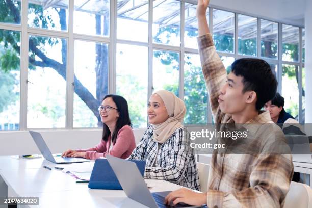 young university student raising hand during a lecture in the classroom. - headscarf stock pictures, royalty-free photos & images