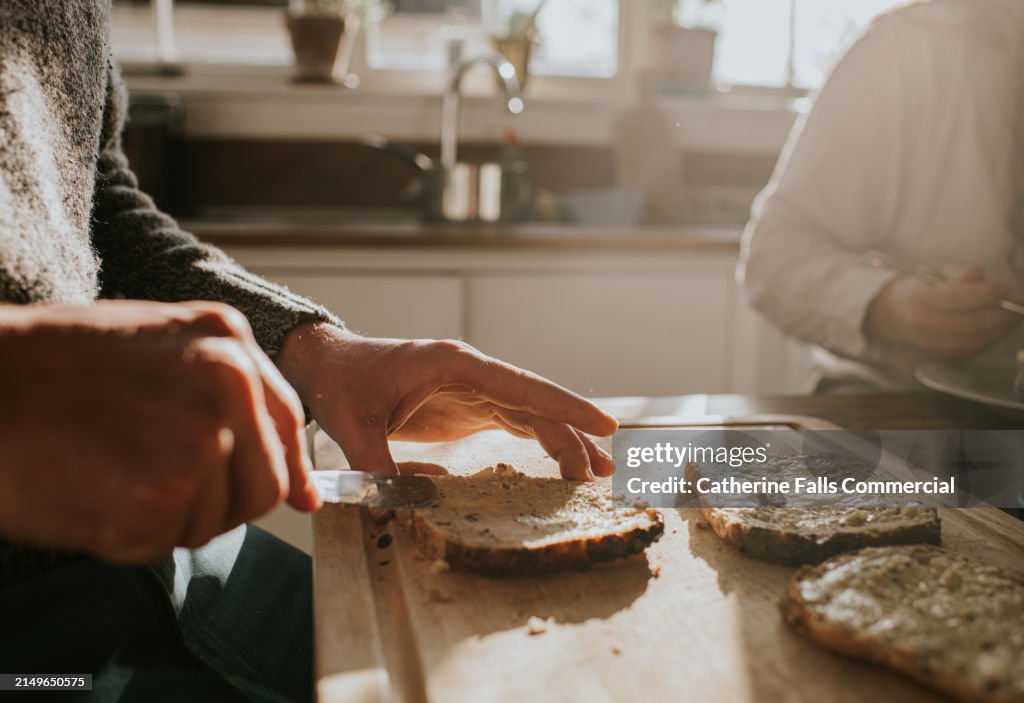 Close-up breakfast scene of a man spreading butter on lightly toasted bread