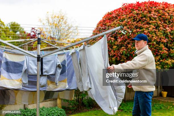 mid adult man taking fresh laundry from the clothesline - draped stock pictures, royalty-free photos & images
