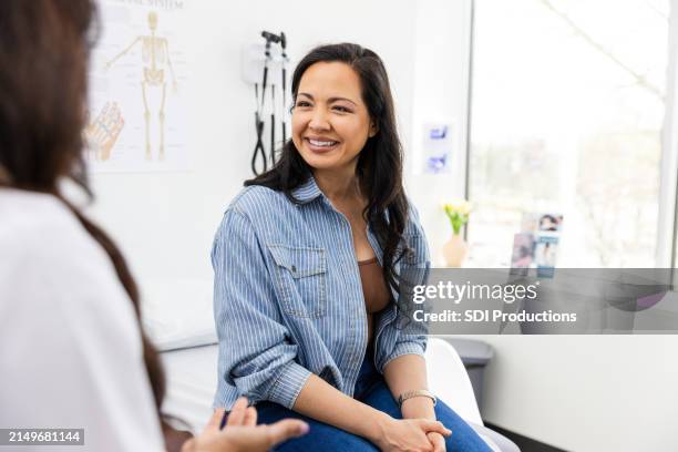 mid adult female patient smiles while listening to the unrecognizable female doctor - cuidados de saúde primários imagens e fotografias de stock