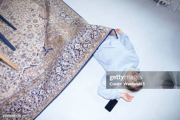 tired woman sleeping by smart phone on floor under carpet in living room at home - exzentrisch stock-fotos und bilder