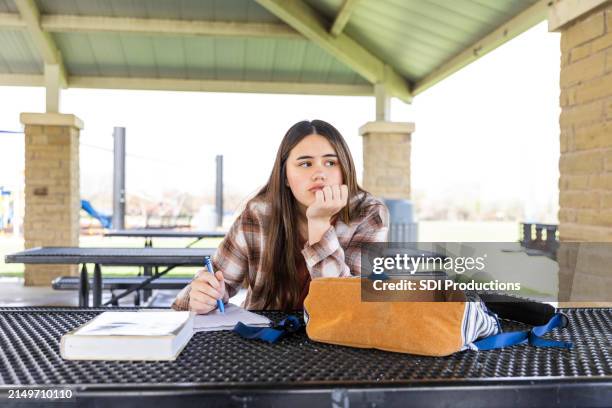 upset young adult female high school student sits alone at the park - struggle stock pictures, royalty-free photos & images
