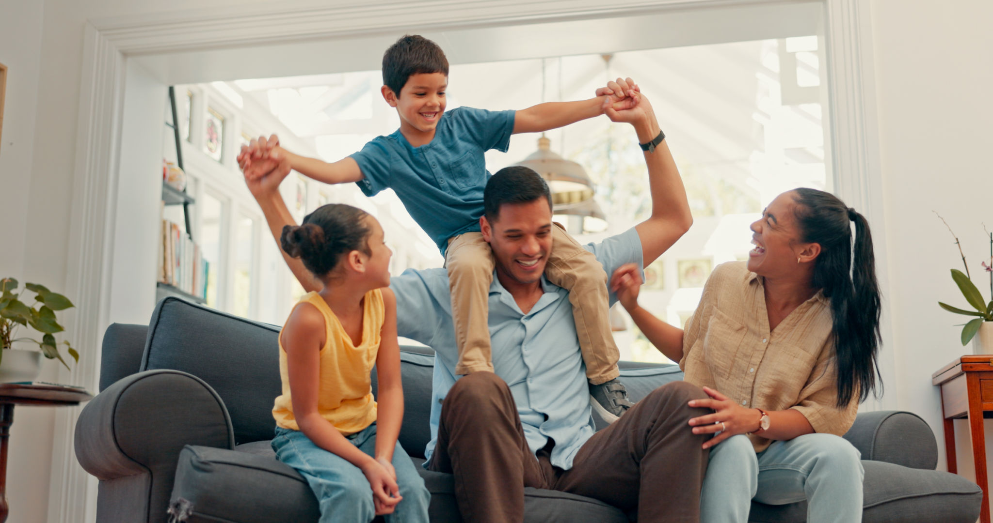 Happy family, love and airplane fun on a sofa with care, security and support while bonding at home. Flying, balance and excited kids with parents in a living room for playing shoulder games together Happy family, love and airplane fun on a sofa with care, security and support while bonding at home. Flying, balance and excited kids with parents in a living room for playing shoulder games together