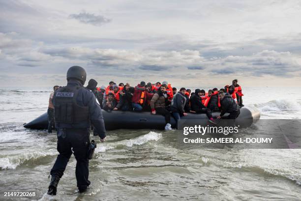 Migrants react as a French police officer stands by ready to puncture the smuggler's boat with a knife to prevent migrants from embarking in an...