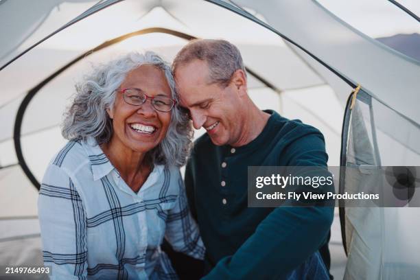 smiling senior woman sits with husband in a tent while camping - baby boomer stock pictures, royalty-free photos & images