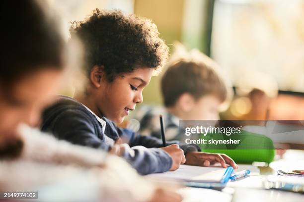 écolier noir souriant écrivant sur une classe à l’école primaire. - écolier-garçon photos et images de collection