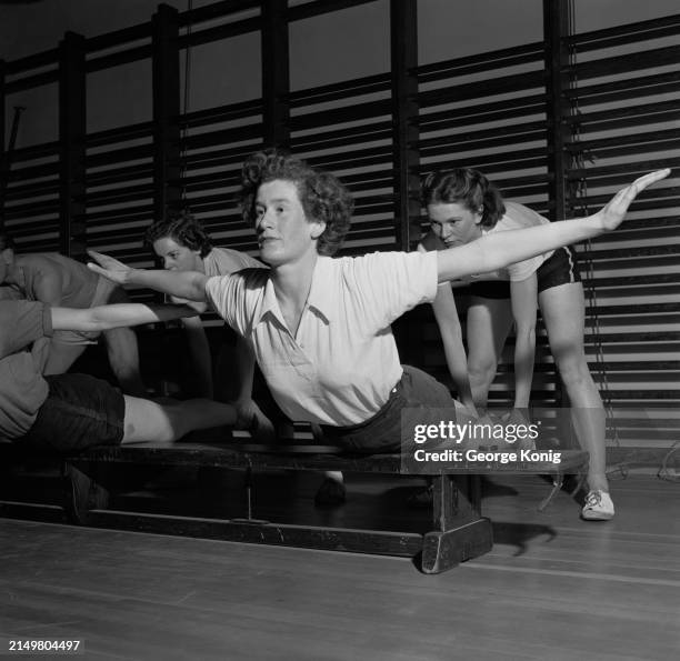 Sprinter Barbara Foster holds the feet of Sheila Lerwill, the world high jump champion, as she exercises at a school gymnasium in Streatham, London,...