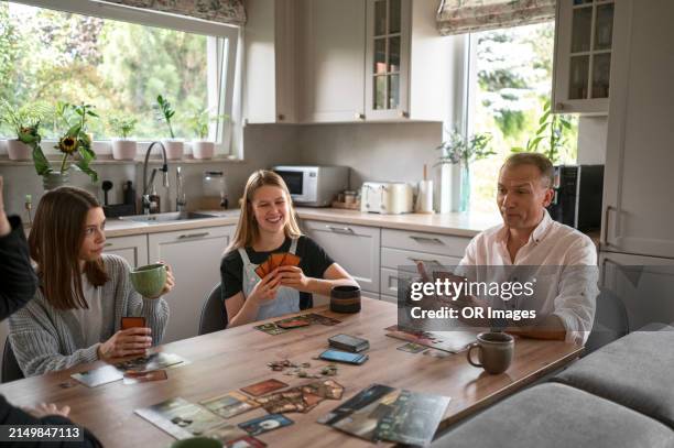happy family playing game at kitchen table at home - bordspel stockfoto's en -beelden