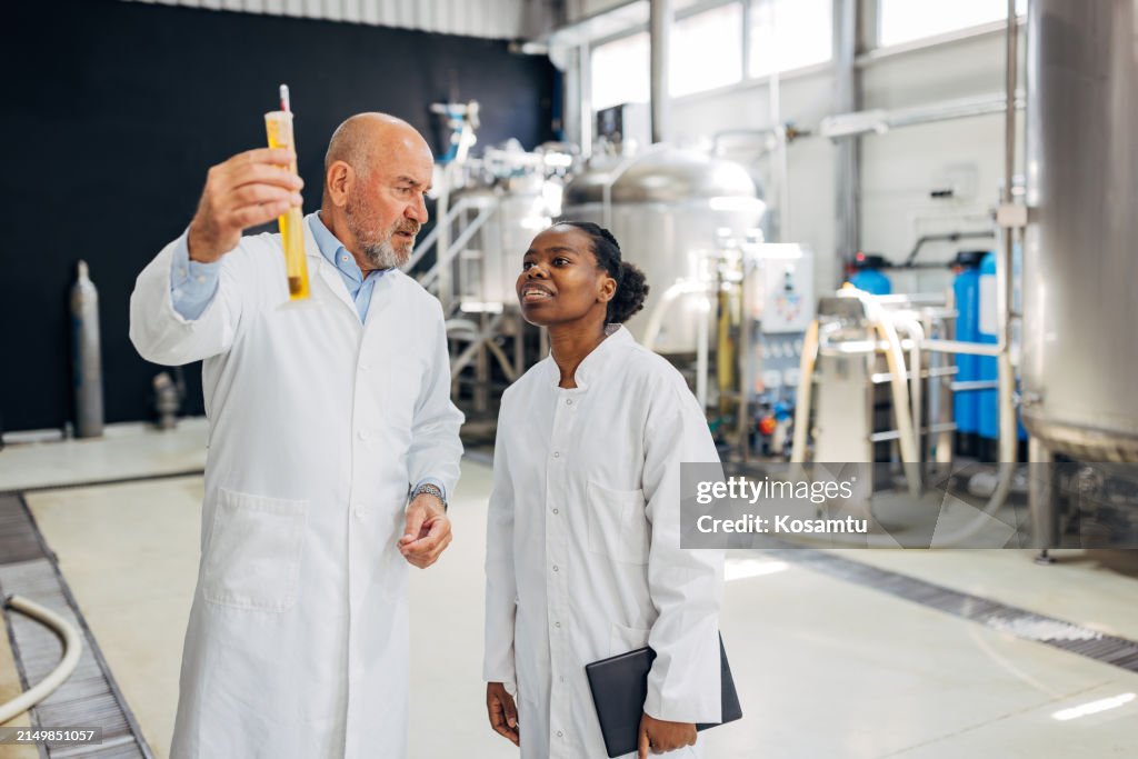 A female brewery technologist learns from a senior brewery expert how to measure the amount of alcohol in beer using a graduated cylinder
