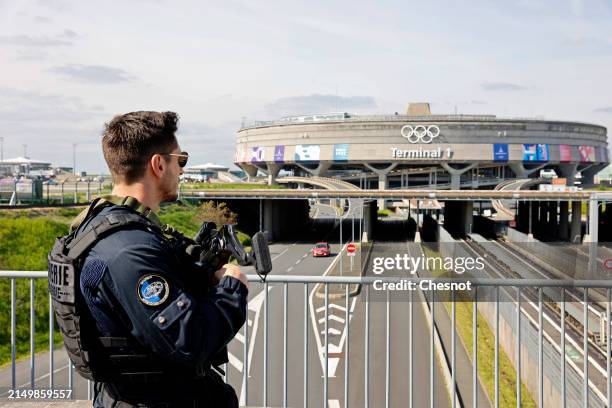 French Police officer stands guard in front of the Terminal 1at Roissy-Charles de Gaulle Airport during an unveiling ceremony of the Olympic Rings on...