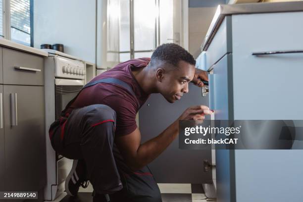 african american handyman at customer's home - looking under sink stock pictures, royalty-free photos & images