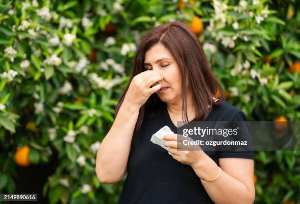 woman with spring allergy sneezes in front of orange trees - spring allergies stock pictures, royalty-free photos & images