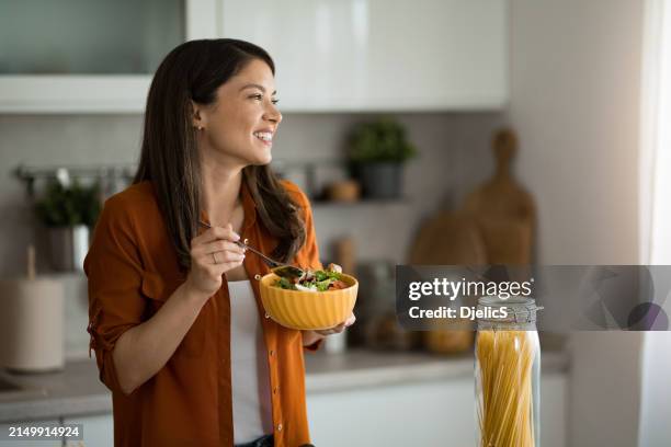 frau isst einen salat in der küche. - gesundes essen stock-fotos und bilder