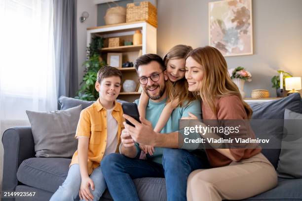 family sitting on sofa looking at mobile phone - family stock pictures, royalty-free photos & images