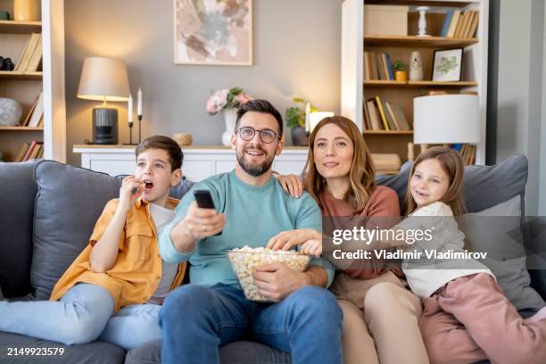 famiglia felice con popcorn e telecomando per l'ora del film - guardare la tv foto e immagini stock
