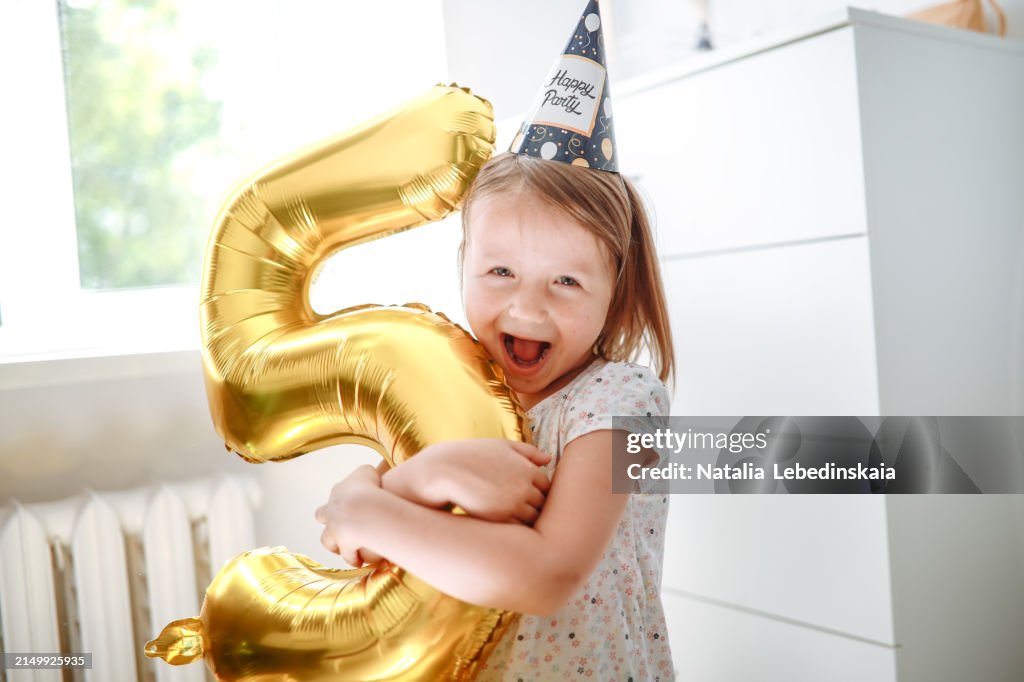 Sweet Happy child, 5 years old, cuddling number 5 balloon on her birthday, celebrating daughter's fifth year