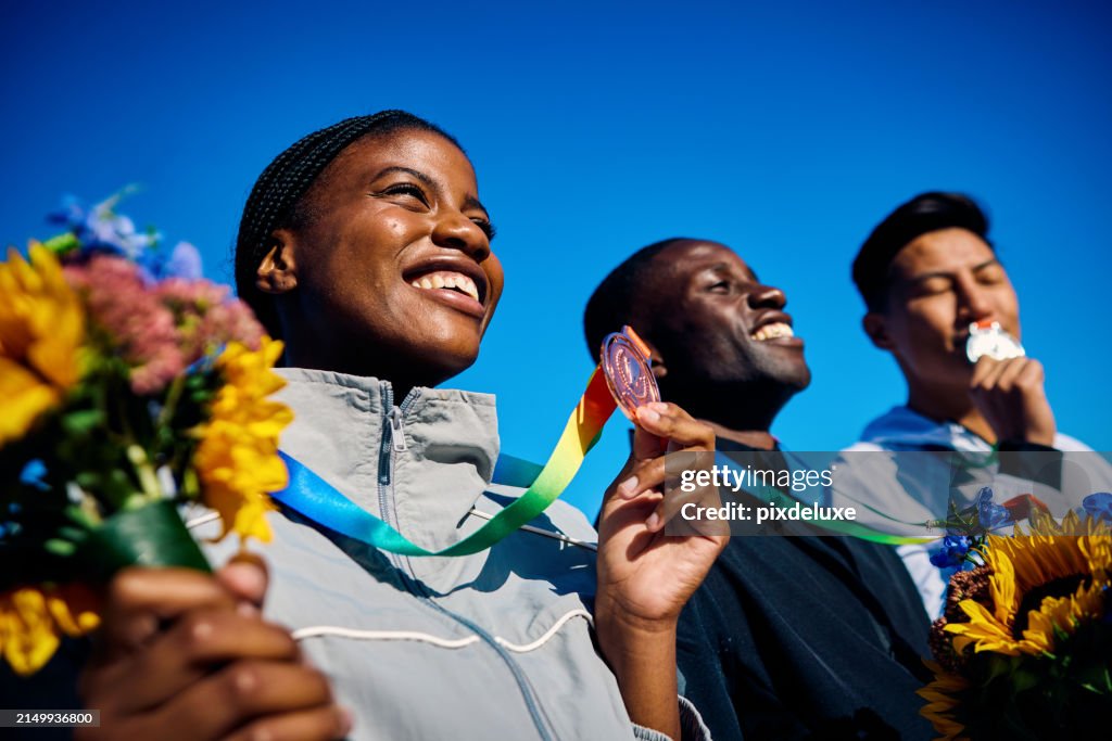 Gruppe internationaler Athleten mit Medaillen und Blumensträußen, die den Sieg feiern. Teamerfolg Outdoor-Porträt unter blauem Himmel. Konzept der multikulturellen Einheit und des Sportsgeistes.