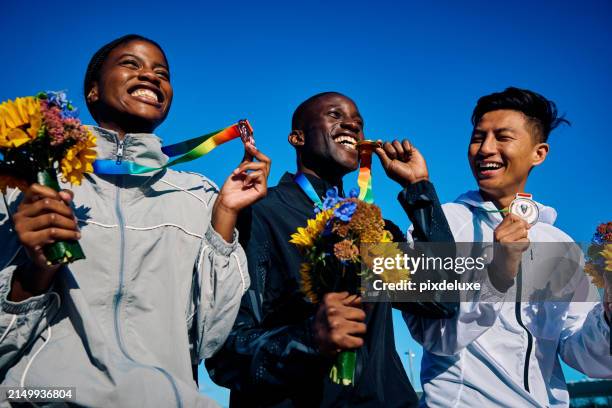gruppe von olympischen athleten mit medaillen und blumensträußen, die den sieg feiern. teamerfolg outdoor-porträt unter blauem himmel. konzept der multikulturellen einheit und des sportsgeistes. - internationales sportereignis stock-fotos und bilder
