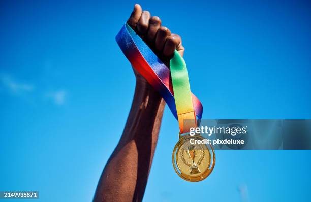 raised hand holding a gold medal against blue sky. victory and achievement concept. - olympische spelen stockfoto's en -beelden