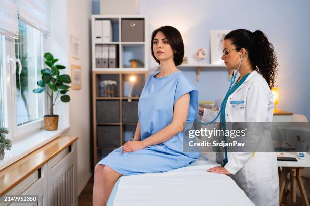 female caucasian doctor examining female patient lungs with an stethoscope - examination table stock pictures, royalty-free photos & images