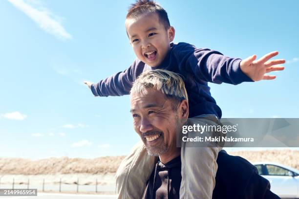 boy is carried on his father's shoulders, his arms outstretched like an airplane. - east asia stock pictures, royalty-free photos & images