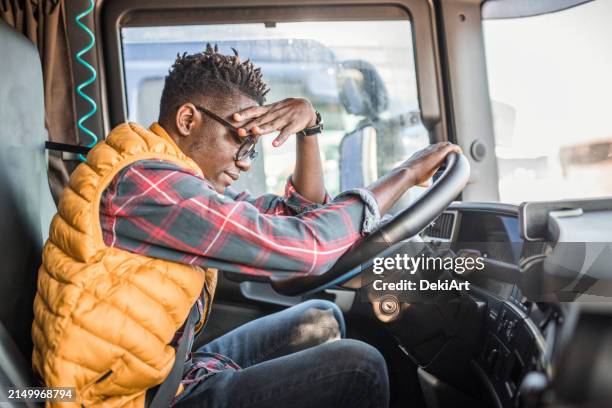 a male truck driver is sitting in the driver's seat of the truck, leaning on the steering wheel. he has a headache - cut off flannel shirt stock pictures, royalty-free photos & images