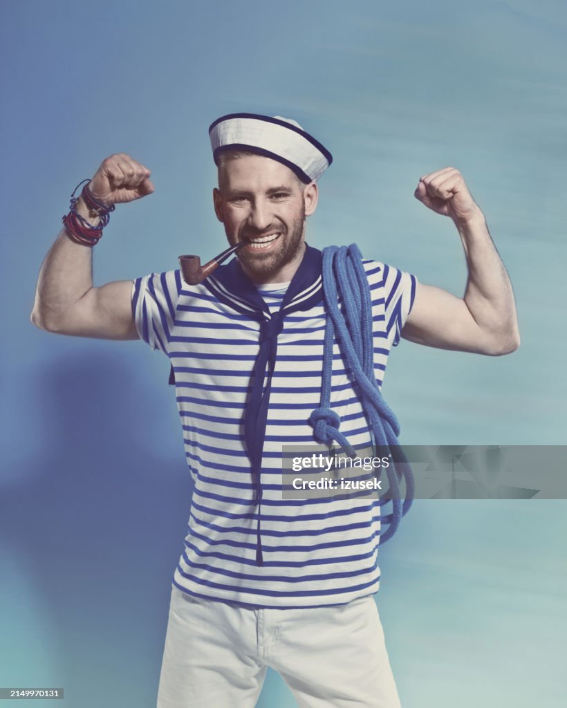 Bearded sailor man smoking pipe and flexing his arms