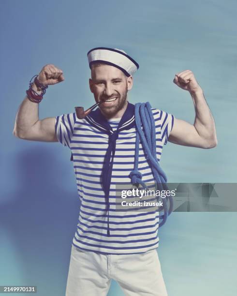 bearded sailor man smoking pipe and flexing his arms - sailor suit stock pictures, royalty-free photos & images