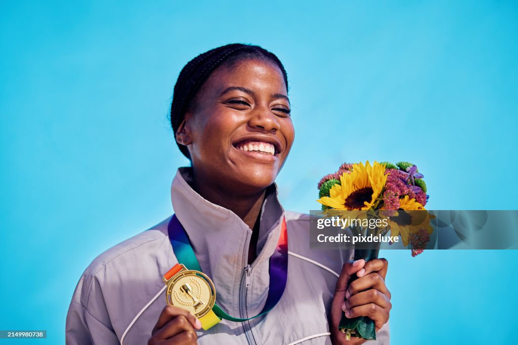Joyful athlete with medal and colorful bouquet of flowers. Outdoor celebration portrait with blue sky backdrop.