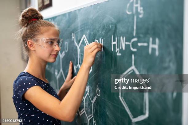 cute teenage girl writing chemical formulas on the blackboard - young inventor stock pictures, royalty-free photos & images