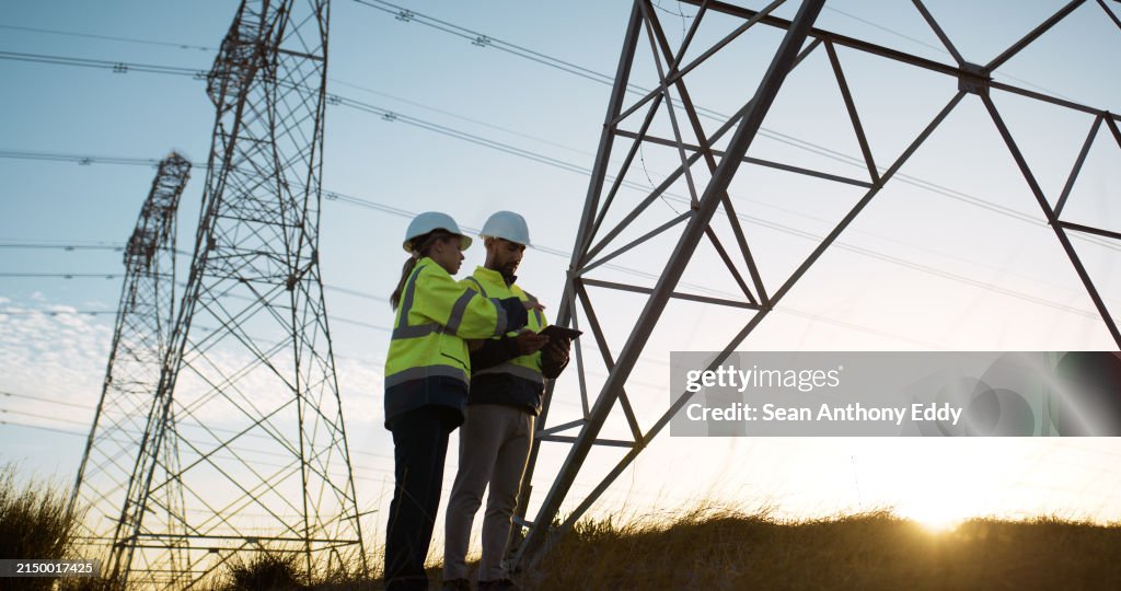 Teamwork, electrical engineer and tablet in power plant with inspection for electricity transmission or tower check. Engineering, collaboration or data transfer for energy distribution or maintenance