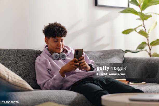 teenage boy with smartphone relaxing on living room sofa - 18 years old boy stock pictures, royalty-free photos & images
