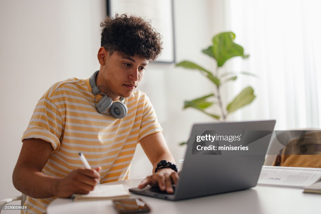 Young Man Studying at Home with Headphones and Laptop