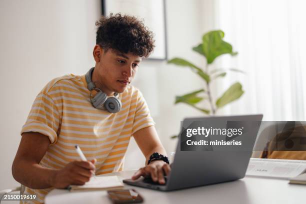 young man studying at home with headphones and laptop - estudos imagens e fotografias de stock