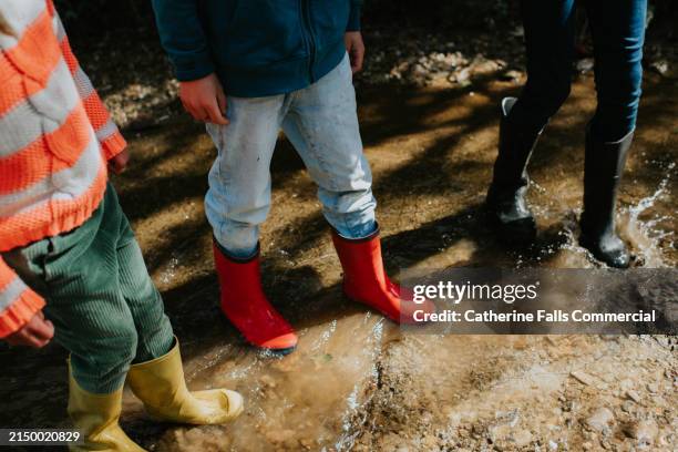 close-up of children jumping in a deep puddle wearing brightly coloured wellington boots - boot stock pictures, royalty-free photos & images